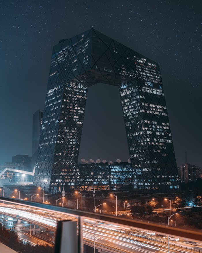 Illuminated CCTV Headquarters in Beijing captured at night with city lights and traffic below.