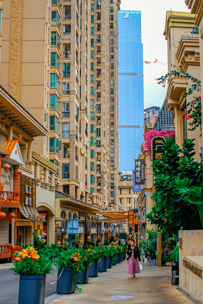 Bustling alleyway with greenery and shops in a modern Chinese cityscape.